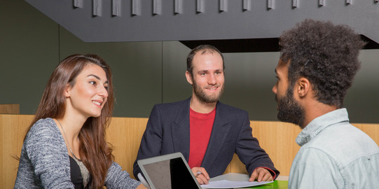 Drei Studierende sitzen sich gegenüber und unterhalten sich.